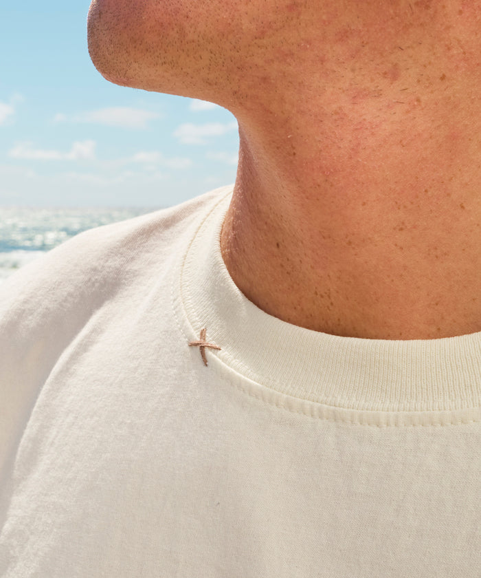 Original Tee (Cream) close-up worn by a person beside the ocean